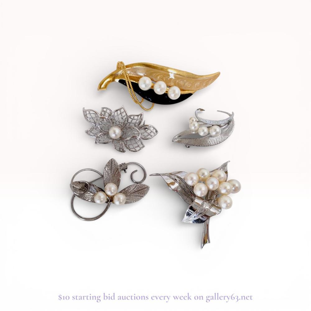 Description
This collection of five botanical-themed brooches includes a sterling silver sprig brooch marked with the Mikimoto M-in-shield hallmark and an S for silver. The assortment features various leaf and floral motifs in silver-tone and gold-tone metals set with cultured and faux pearls. Construction techniques include filigree openwork, textured metal casting, and bi-color enamel application, all featuring safety pin clasps.
Dimensions: 4 cm to 9 cm length.