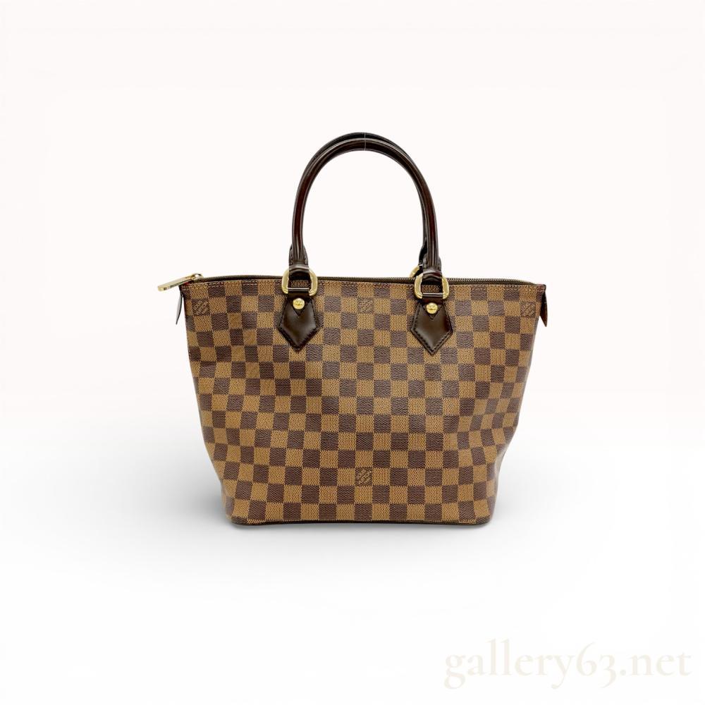 Description
Louis Vuitton Saleya PM tote bag in Damier Ebene coated canvas with dark brown leather trim. The exterior features the signature checkerboard pattern and gold-tone hardware, while the interior is lined in red Alcantara with two slip pockets. The bag includes rolled leather handles, a zip-top closure with a logo-embossed pull, and an interior leather tab stamped Louis Vuitton Paris made in France.
Base width approximately 10.25 inches (26 cm).