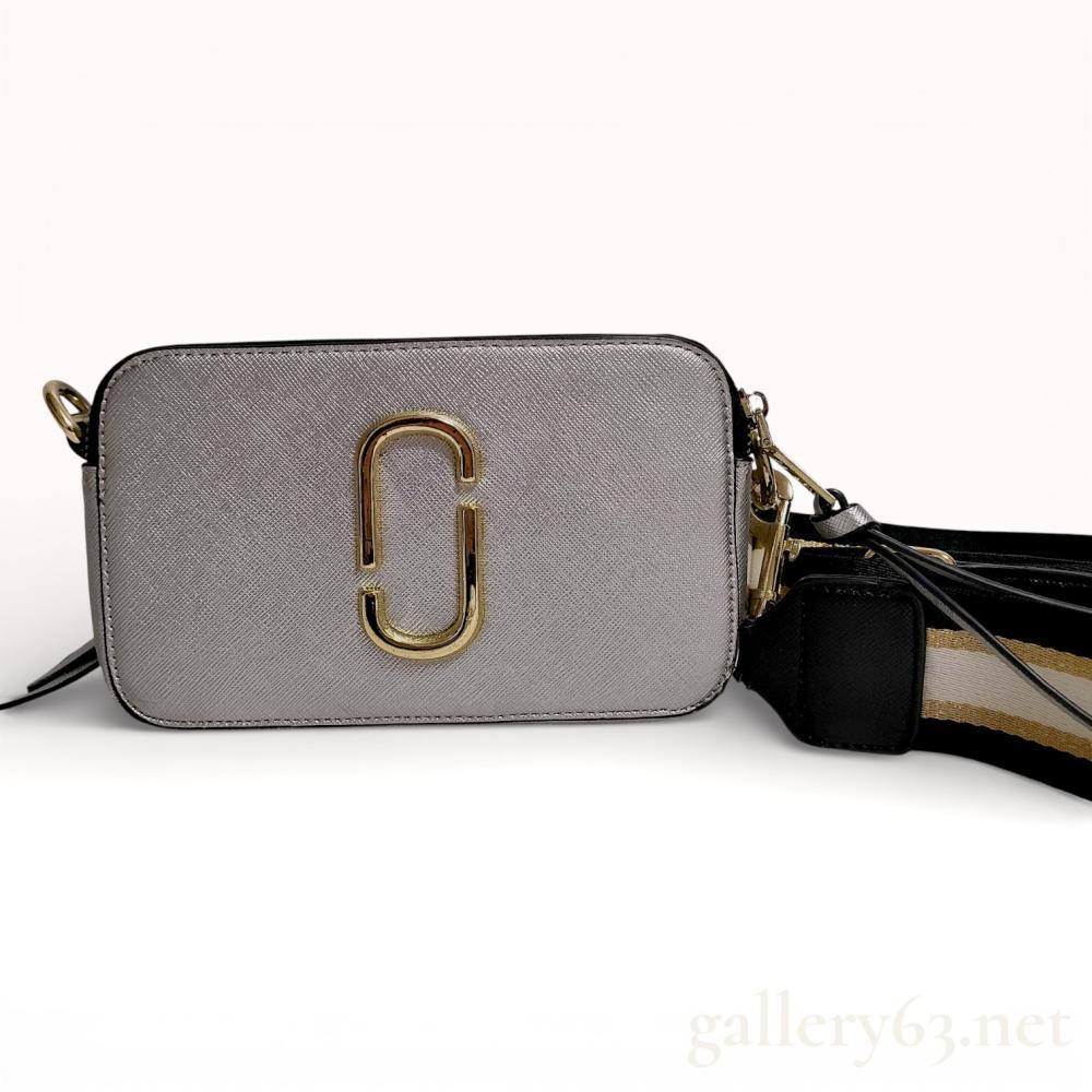 Description
Marc Jacobs Snapshot camera bag in metallic silver Saffiano leather. The compact rectangular design features dual independent zippered compartments, an exterior rear slip pocket, and signature gold-tone Double J hardware. Includes a detachable and adjustable black, white, and metallic gold striped webbing strap with gold-tone lobster claw clasps. The top leather panel is embossed MARC JACOBS NEW YORK.
7.5 inches W x 4.25 inches H x 2.3 inches D.