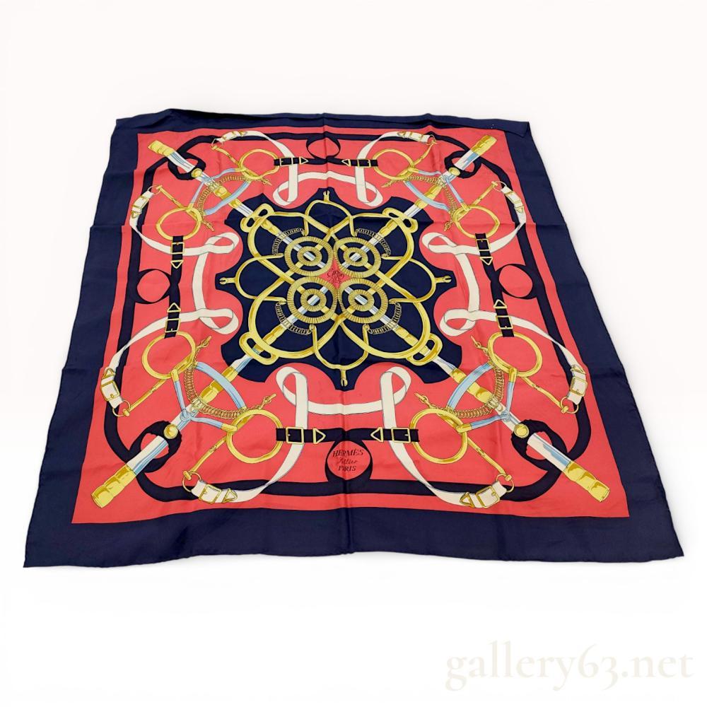 Description
Hermes silk twill scarf in the Eperon d’Or pattern designed by Henri d’Origny, late 20th century. The equestrian-themed design features bits, spurs, and leather straps in gold and white against a vibrant red field and navy blue border. It includes a circular Hermes Sellier Paris emblem, the pattern title in script, and a copyright mark on the hand-rolled edge.
Approximately 35 x 35 inches.