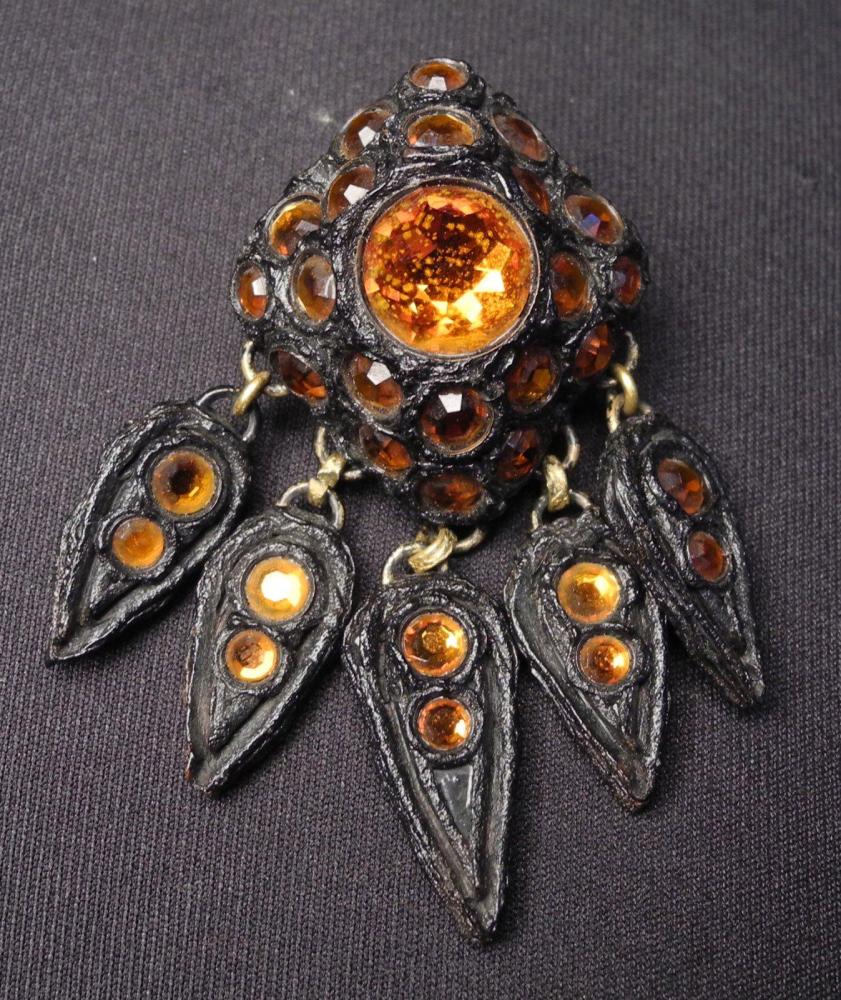 HENRY - circa 1960

Broche de forme losangique en résine noire gravée rehaussée de strass oranges se finissant pas des pendeloques Signé