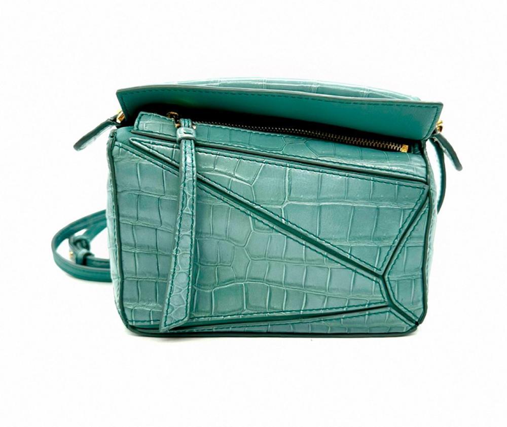 Description

LOEWE.
Puzzle bag.
Crocodile leather in a refined blue-green tone that accentuates its sophisticated and exclusive character. Gold hardware.
Includes detachable shoulder strap for greater versatility, allowing it to be worn over the shoulder or across the body.
As new. Measurements: 10 x 17 x 8 cm.

This compact bag retains all the elegance and functionality of the Puzzle model, a revolutionary creation launched by Jonathan Anderson in 2014, recognized for its geometric lines and precise construction.