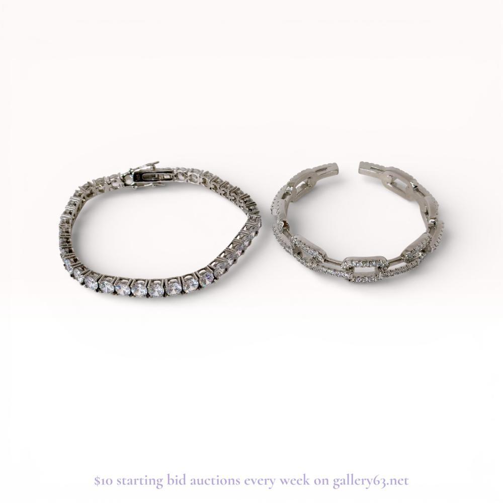 Description
Two silver-tone bracelets including a sterling silver tennis bracelet and a chain-link motif cuff. The tennis bracelet features round-cut clear stones in four-prong basket settings with an integrated box clasp and dual safety latches. The open cuff bangle displays an interlocking link design accented with pave-set clear stones. The tennis bracelet is marked 925 on the interior of the clasp.