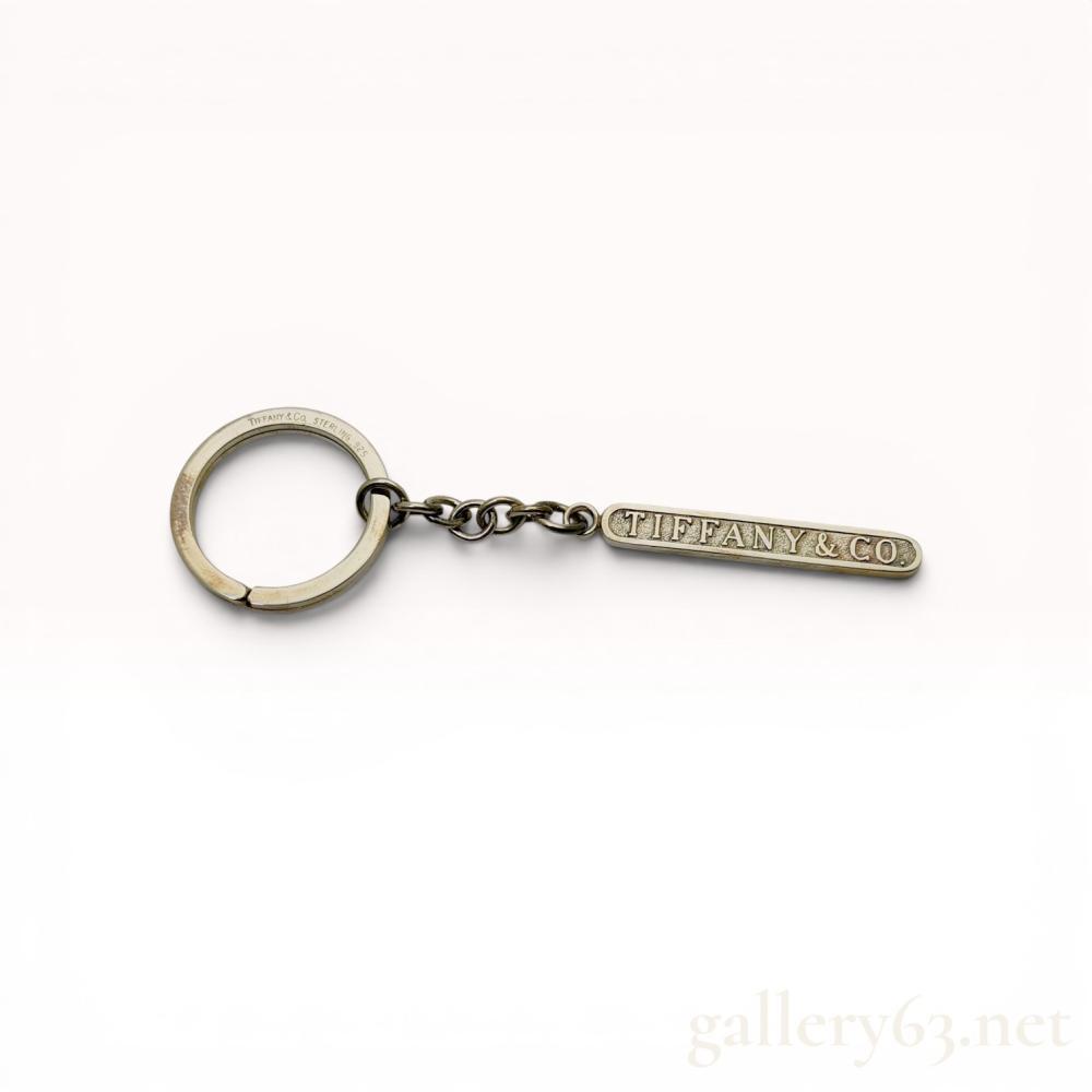 Description
Tiffany & Co. sterling silver keychain featuring a rectangular bar charm. The split ring is connected by a cable link chain to the bar, which is embossed with the maker name. Hallmarks include TIFFANY & Co. STERLING 925 on the ring and 925 on the reverse of the charm. Accompanied by a signature blue box and fabric pouch.
Length: Approximately 10.5 cm.