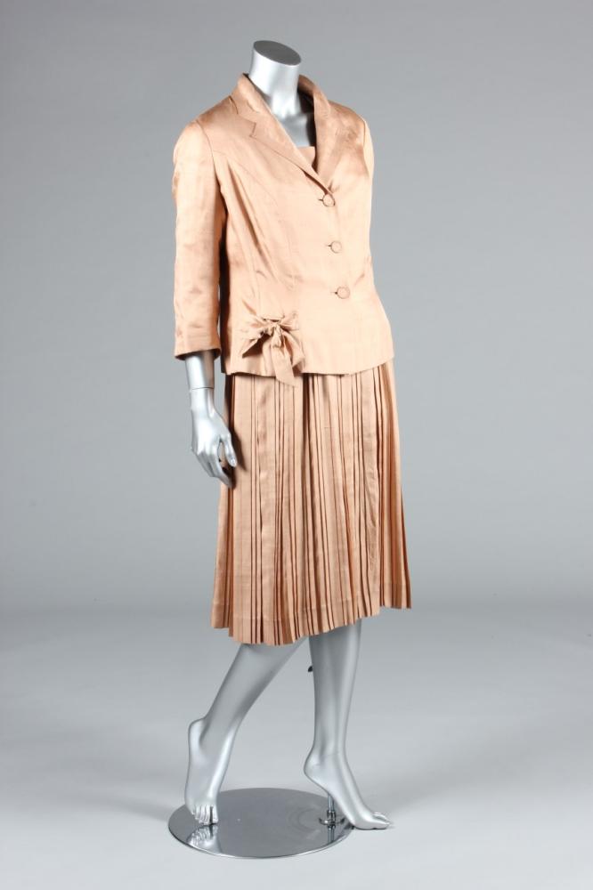 

A Maggy Rouff couture old-rose shantung silk ensemble, late 1950s, with London-Paris label, the short sleeved dress with top-stitched edging, two bows to the bodice above finely pleated skirt; the matching jacket with contrasting polka-dot lining, large bow ties to the pockets, bust 102-107cm, 40-42in, waist 71cm, 32in (2)
