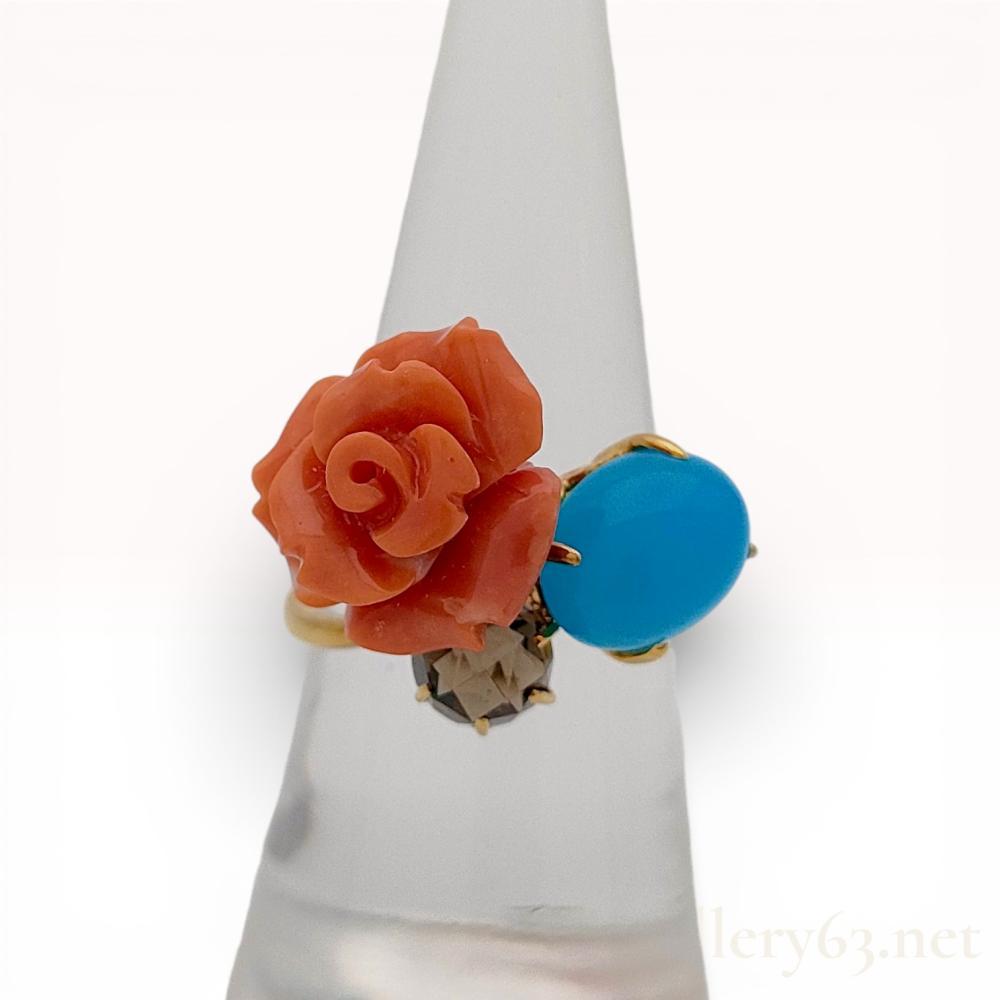 Description
An 18K yellow gold multi-stone cocktail ring featuring an asymmetrical cluster design. The setting includes a salmon-colored antique coral specimen carved into a blooming rose, a robin’s-egg blue turquoise cabochon in a decorative openwork basket, and a faceted smoky quartz in a claw setting. The interior of the polished gold shank is hallmarked K18. 
Ring size approximately US 7