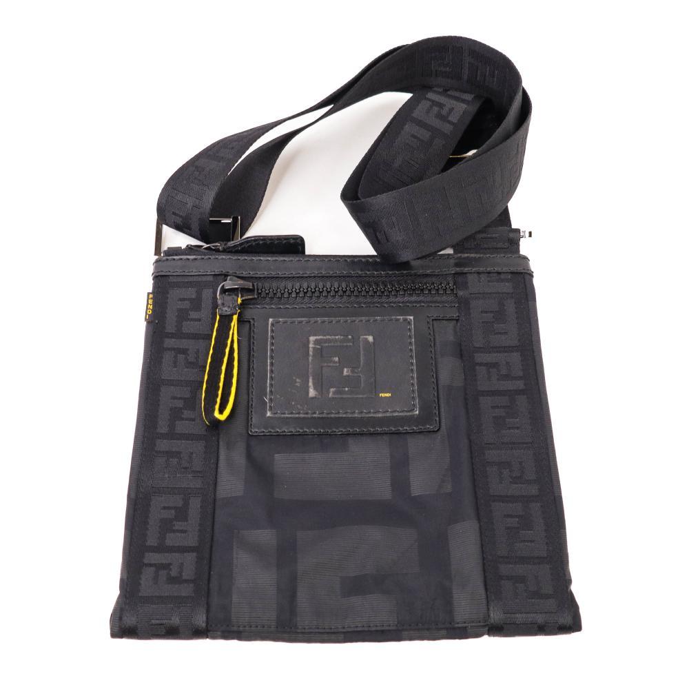 Description
Fendi flat messenger bag in black tonal Zucca monogram technical fabric with leather trim. The front features an embossed leather double-F logo patch with yellow Fendi branding, a horizontal zipper pocket with a yellow pull-tab, and a side fabric logo tag. It is fitted with an adjustable wide webbing shoulder strap displaying a repeating FF logo pattern and gunmetal-tone hardware.