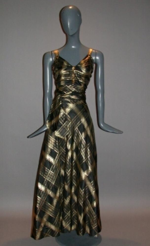 Mainbocher Gold and Black Plaid Silk Evening Gown

Lot 526
Mainbocher Gold and Black Plaid Silk Evening Gown
 French, circa 1940 
 With sweetheart line camisole bodice, two triangular inserts defining waist, flared skirt gathered at back, plaid matched at all seams, three decorative oval buttons, zipper colored to match fabric, self corsage flower, separate sash, size 8-10, labeled: Mainbocher/12 Avenue George V/A Paris/Made In France and written tape label: Wanamaker 75 Robe 620.2965.
Good condition, sash possibly taken from hem, some discolorations at armscyes and oxidation of gold.