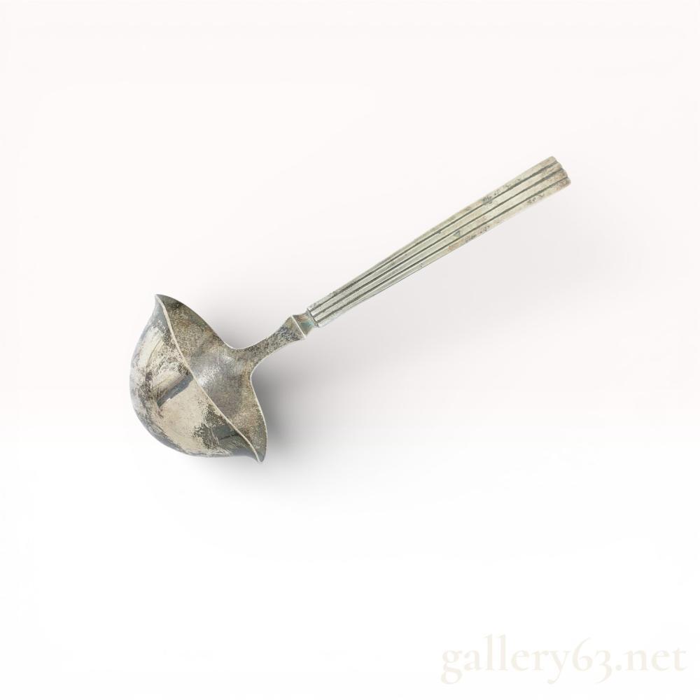 Description
Georg Jensen soup ladle having deep rounded bowl with broad pouring lip and smooth curved interior. Bowl connected to long tapered handle with raised central ridge and parallel line detailing running along length. Handle presenting slight outward flare near terminal end.
Neck area showing distinct angular shaping where handle meets bowl. Reverse of handle stamped with Georg Jensen hallmark and 925 silver mark. Ladle measuring approximately 20 cm in length based on scale image.

Artist or Maker
Georg Jensen