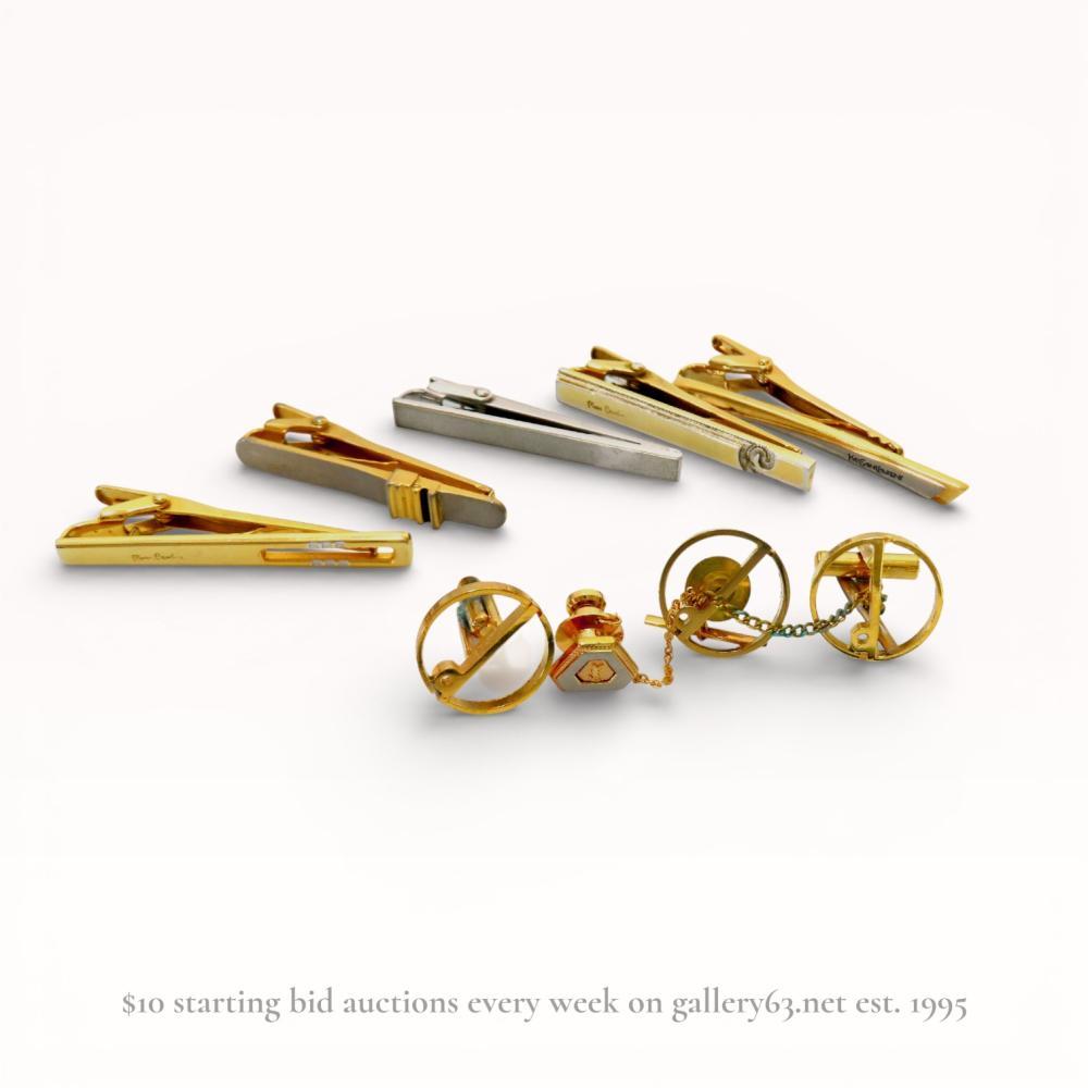 Description
A group of men’s fashion accessories including signed pieces by Pierre Cardin and Yves Saint Laurent, mid-to-late 20th century. The collection features multiple tie clips in various gold-toned and silver-toned base metal finishes and a coordinated cufflink and lapel pin set. Notable items include several Pierre Cardin clips with cursive signatures and an Yves Saint Laurent clip with a block letter signature.
Tie clips: approximately 5 cm to 6 cm length.