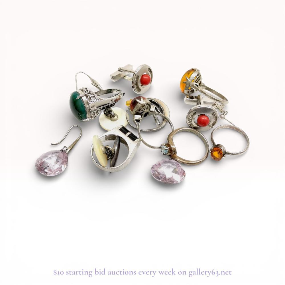Description
An assortment of sterling silver jewelry and gentleman’s accessories including rings, cufflinks, and earrings. Featured items include a filigree ring with a green cabochon, a reddish-brown cabochon ring marked SILVER, and lavender briolette drop earrings marked 925. The group also contains mother-of-pearl chain-link cufflinks, red bead toggle cufflinks, a modernist band with black inlays, and pave-set cross earrings.
