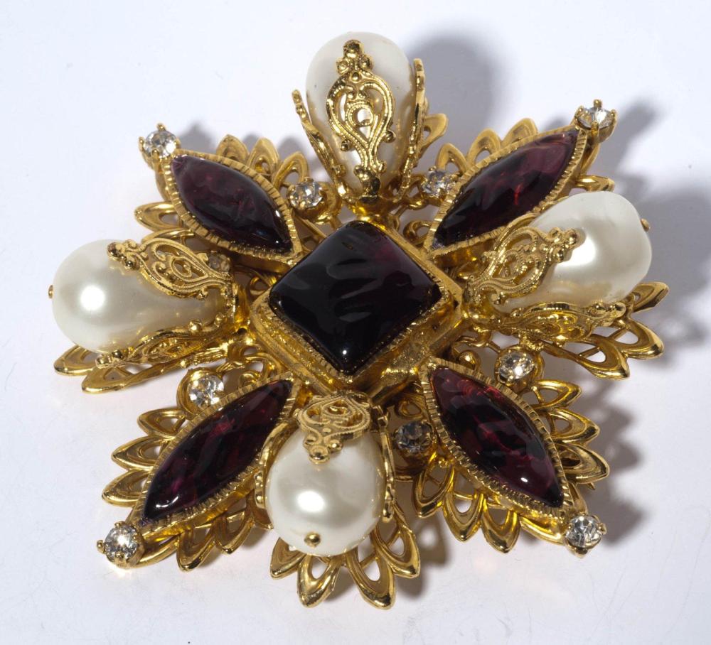 CHANEL

Broche d’inspiration byzantine en métal doré repercé orné de cabochons de résine améthyste rehaussés de perles blanches de forme goutte enchassées de motifs ciselés, repercés, épaulés de strass à l’imitation brillant. Signée