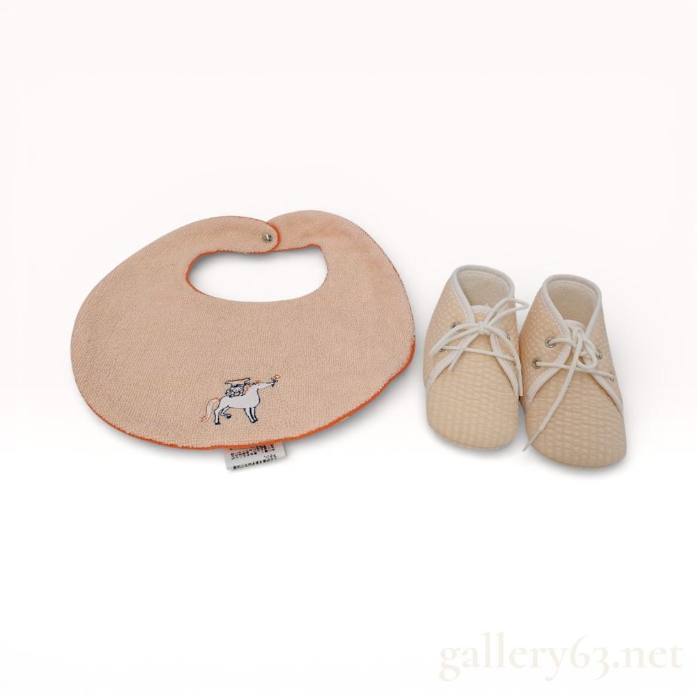 Description
Hermes cotton baby set in the Cabriole pattern, contemporary. The set consists of a round bib with a printed cotton front and terry-cloth reverse, alongside a pair of waffle-knit lace-up booties. Both pieces feature whimsical horse and figure illustrations with signature orange piping and an engraved silver-tone snap closure.
Bib: 22 cm width
Booties: 11 cm length (Approx. US Infant 3 / EU 18).