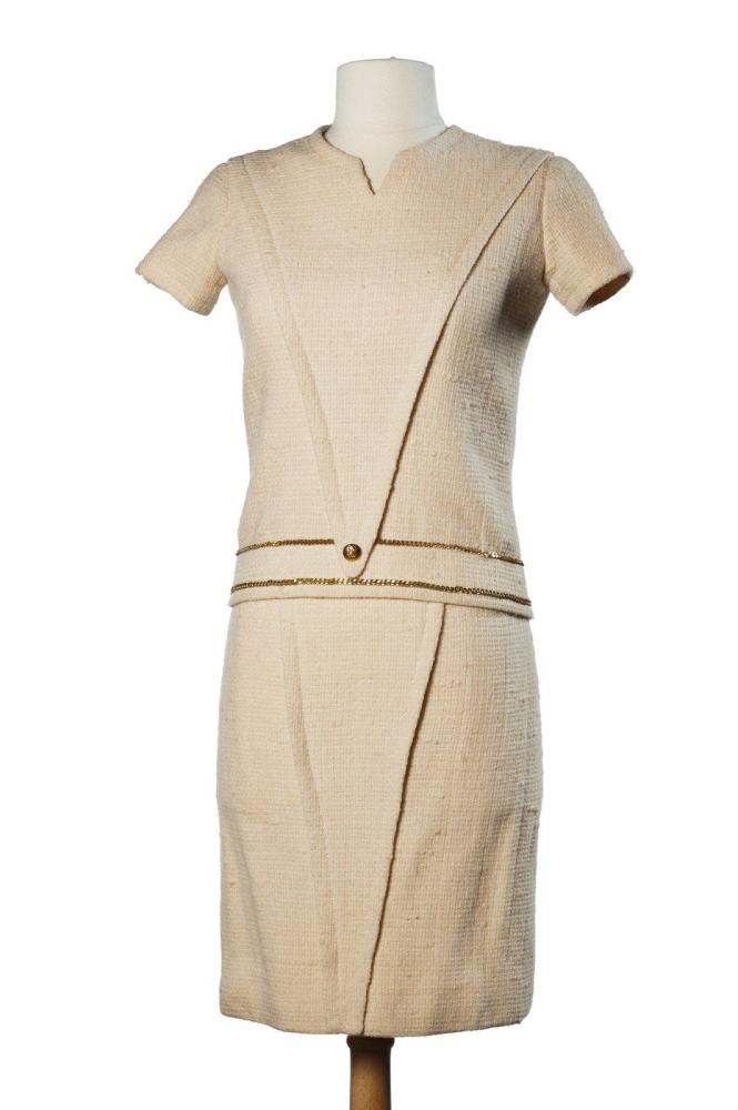 CHANEL

HAUTE COUTURE, CIRCA 1960 Ensemble en tweed écru, haut à effet de découpe triangulaire, ras du cou sur petite échancrure, petites manches, taille soulignée de deux chaînes en métal doré, dos à boutonnage asymétrique, jupe droite à effet portefeuille au dos. Sans griffe