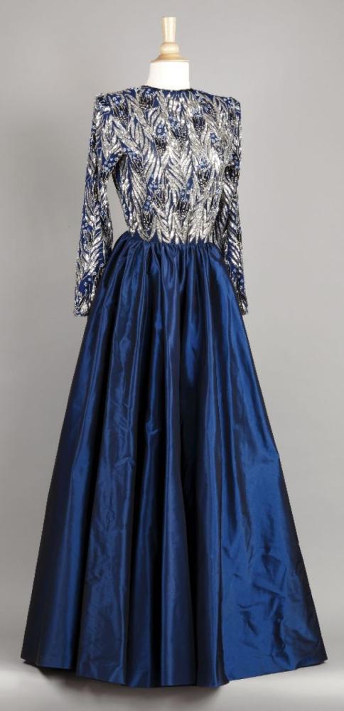 Jean LOUIS SCHERRER haute couture no 002082 circa 1980, broderie Lesage

Robe grand soir, haut en mousseline bleue rebrodée de paillettes argent à motif végétale, de strass entourés de perles de verre figurant des tulipes, encolure bateau sur décolleté au dos, manches longues, jupe ample en taffetas bleu nuit. Griffe blanches, graphisme noir