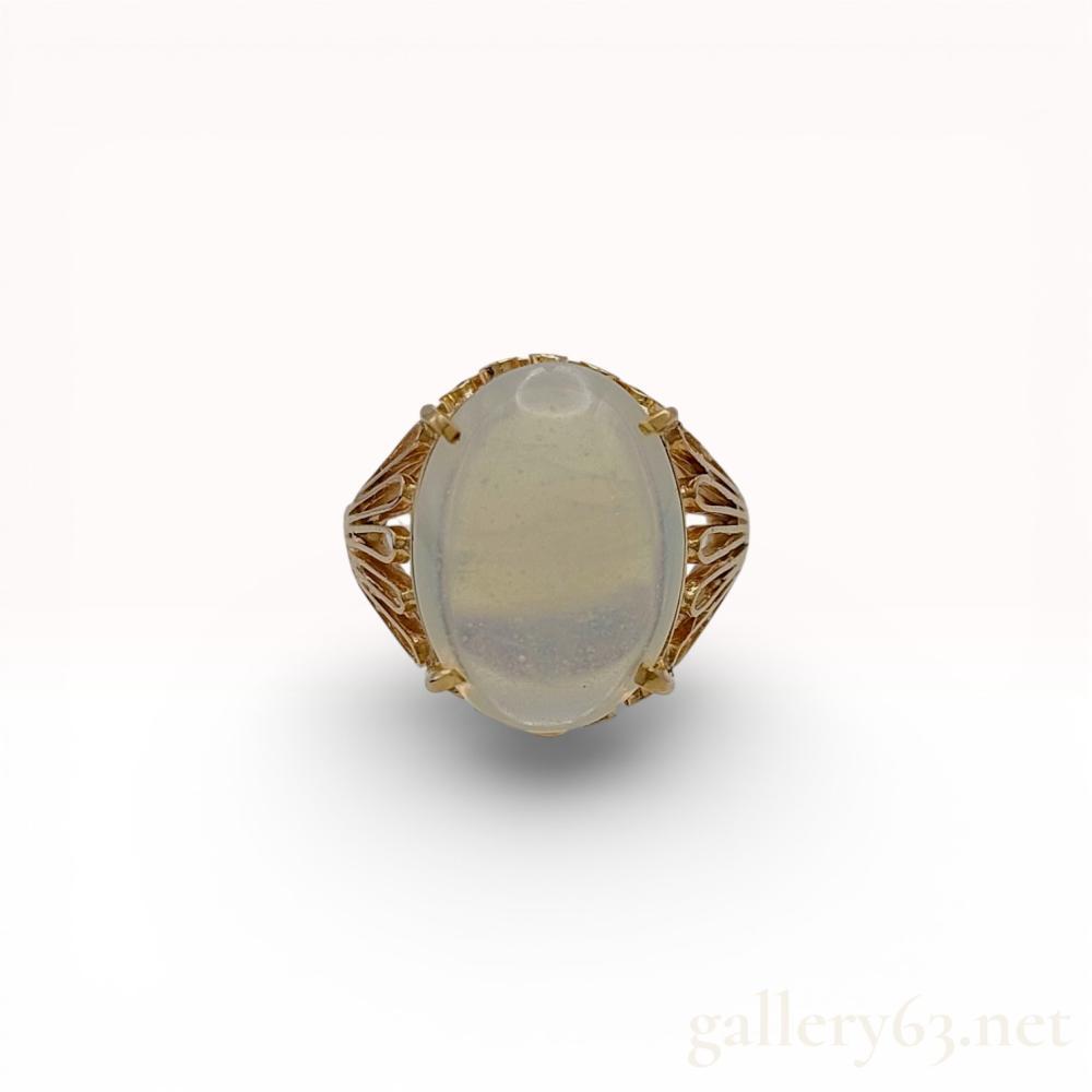 Description
Vintage cocktail ring featuring a large oval cabochon moonstone set in a 14 karat yellow gold mounting. The setting consists of a four-prong head atop an elaborate openwork gallery with filigree scrollwork and feathered radial shoulders. The interior of the band contains a recessed 14K hallmark indicating gold purity.
Size: US 6.5 / 53.