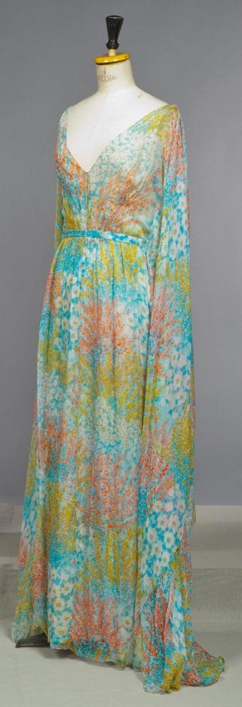 CHANEL

Haute couture, circa 1970 Robe du soir longue en mousseline de soie imprimée à motif abstrait multicolore, décolleté en pointe, sans manches, panneaux de chaque côté donnant un effet de cape, jupe souple, taille soulignée d’une ceinture à nouer au dos. Griffe blanche, graphisme noir
